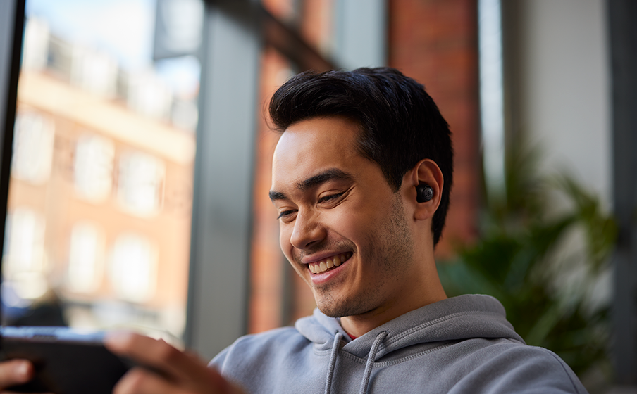 Pessoa usa os fones JBL Quantum TWS Air enquanto segura um dispositivo de jogo